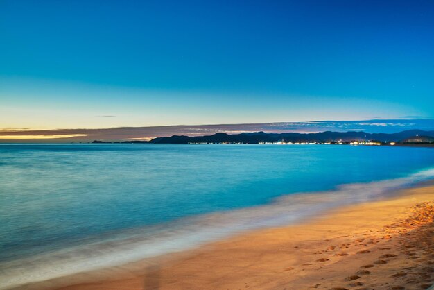 Foto noche en la playa y en el horizonte las luces de un pueblo