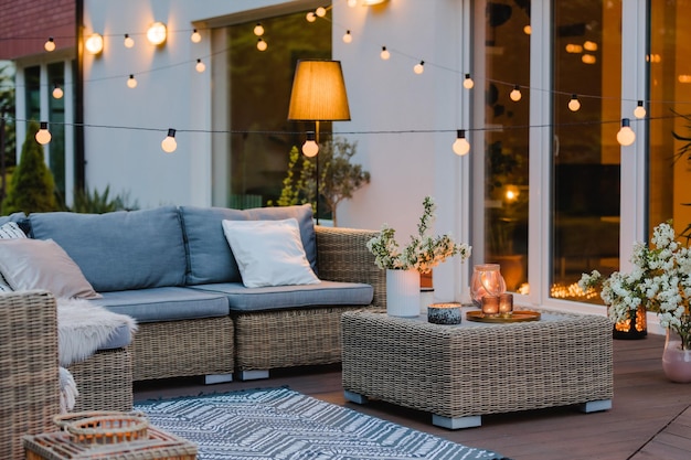 Noche de verano en la terraza de una hermosa casa suburbana con patio con muebles de mimbre y luz