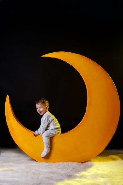 Foto nochebuena. nena, el niño se sienta en una luna amarilla en pijama.