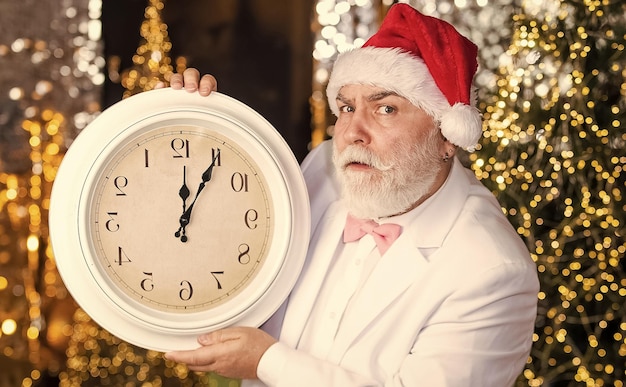 Nochebuena Santa claus contando el tiempo Concepto de medianoche Cuenta regresiva de año nuevo Hombre con reloj retro Fondo de iluminación de Garland Empresario barbudo con sombrero de santa Hombre mayor de santa en esmoquin