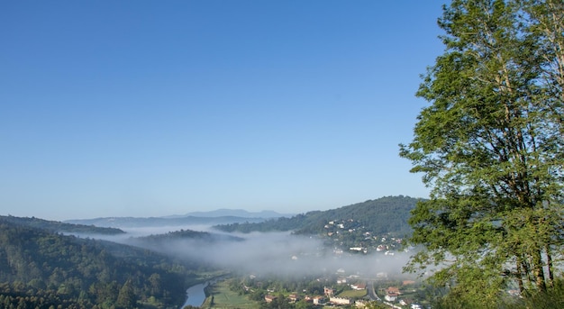 nördlicher Berg hoch oben mit grünem Wald und nebligem Dorf, das den Fluss überquert