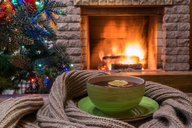 Noite de natal. Lareira aconchegante e uma xícara de chá na mesa de madeira, cachecol quente.