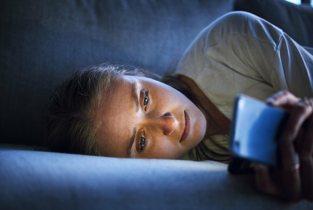 Noite de telefone e mulher triste relaxando no sofá na sala de estar rolando nas mídias sociais após um rompimento Depressão chateada e menina no sofá na sala lendo empréstimos estudantis ou e-mails de dívida no smartphone