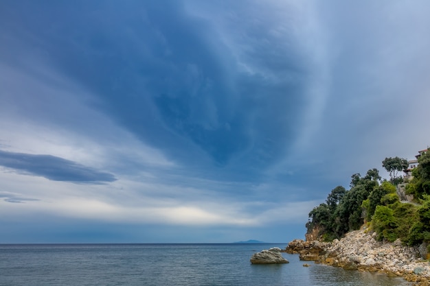 Noite de verão em uma pequena praia rochosa. Mar calmo e construções de pedra entre as árvores na colina