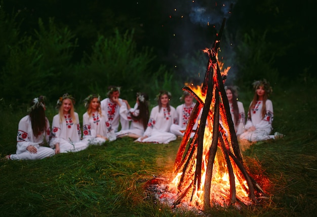 Noite de verão, jovens em roupas eslavas, sentados perto da fogueira.