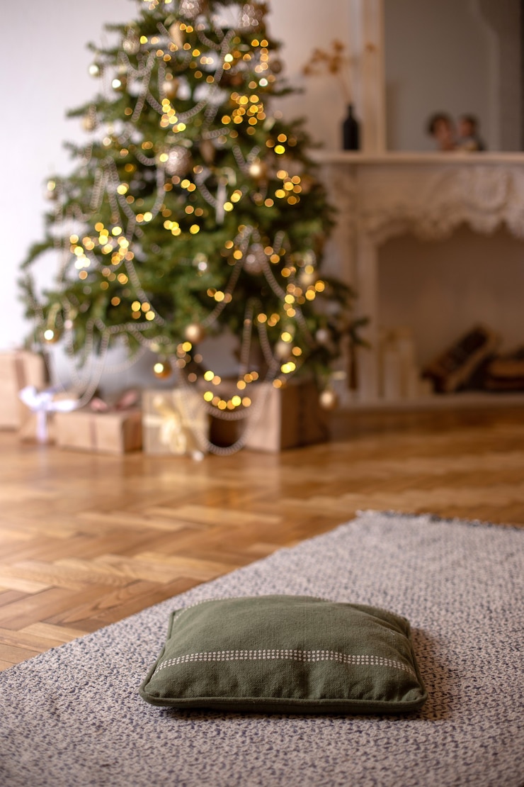 Foto noite interior de ano novo com almofada verde macia no chão, primeiro plano e árvore de natal com guirlandas brilhantes e lareira branca no fundo. vertical