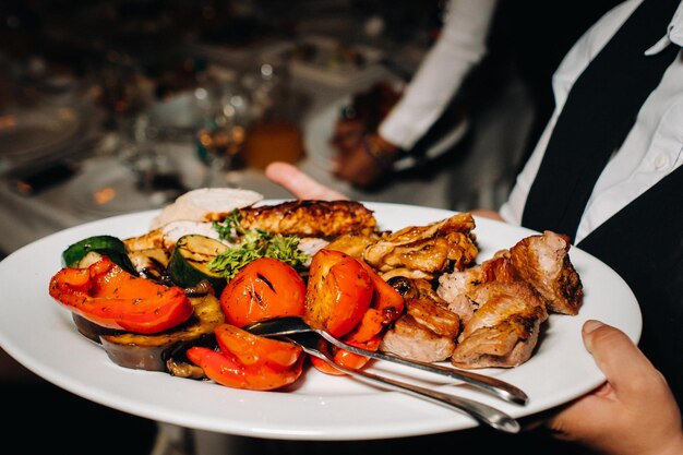 À noite, o restaurante serve um prato quente de churrasco com vegetais carne frita com tomates e outros vegetais em um prato em um restaurante