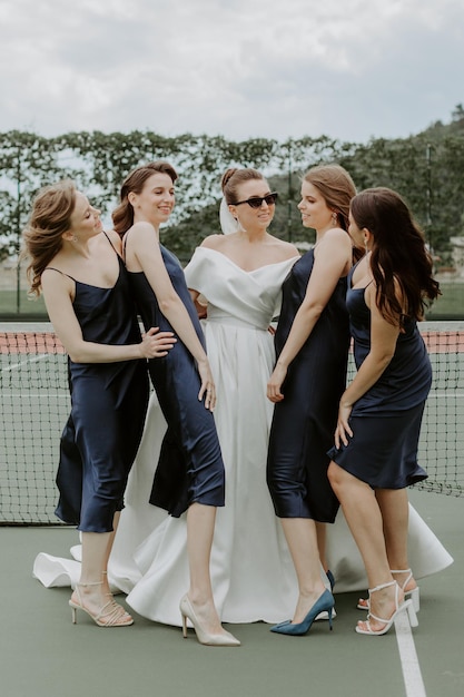Noiva com as damas de honra nos vestidos brilhantes na quadra de tênis