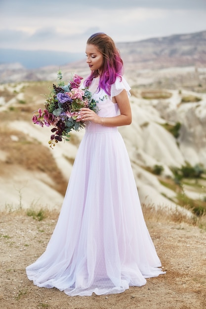 Noiva com cabelo rosa e um longo vestido de noiva segurando um lindo buquê de flores