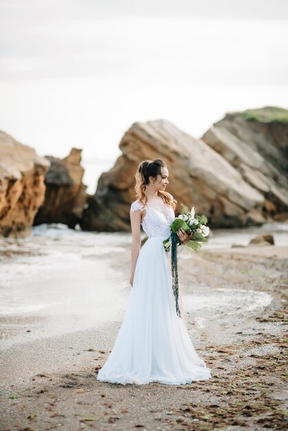 Noiva com um buquê de casamento na costa do mar Negro sob a luz do sol