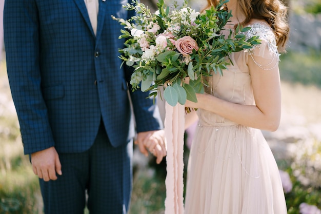 Noiva com um buquê de flores segurando o close da mão do noivo