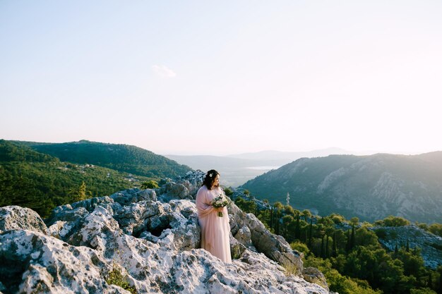 Noiva com um buquê fica nas pedras e olha as montanhas