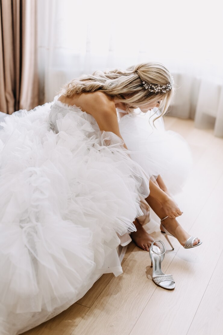 Foto noiva com um vestido longo de tule branco, calçando os sapatos pela manhã.