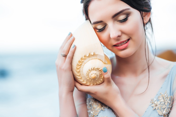 Foto noiva com uma grande concha na praia em um vestido de noiva azul