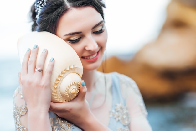 Noiva com uma grande concha na praia em um vestido de noiva azul