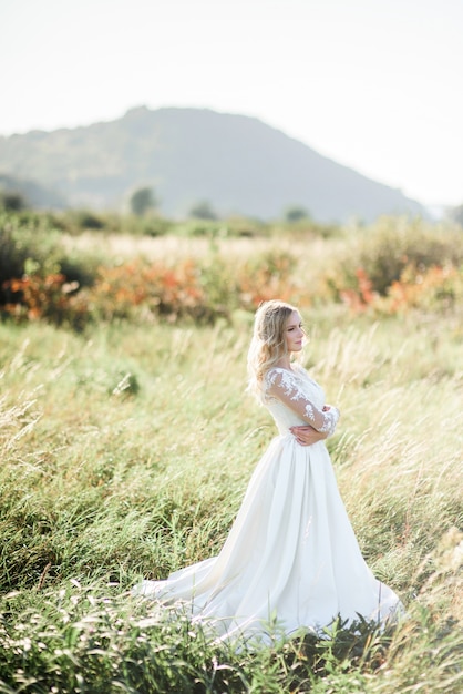 Noiva deslumbrante com cachos brancos fica no campo em um dia ensolarado