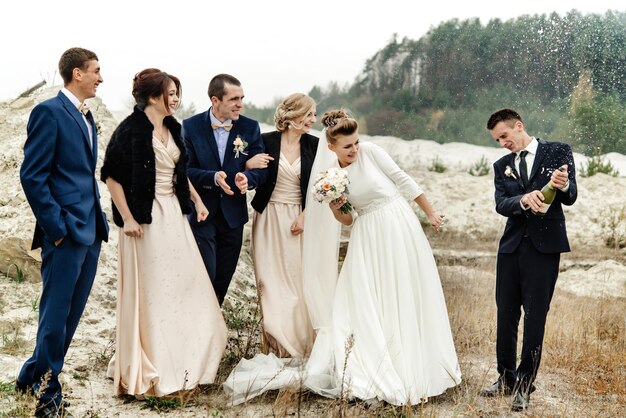 Noiva e noivo com padrinhos e damas de honra felizes se divertindo e estourando champanhe celebração de casamento de luxo momento hilário