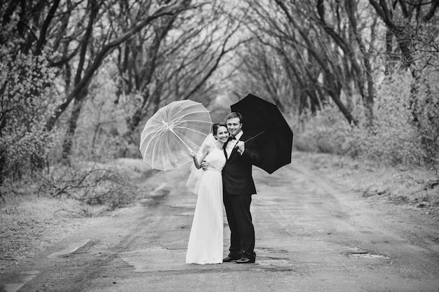 Noiva e noivo em um dia chuvoso de casamento andando sob um guarda-chuva