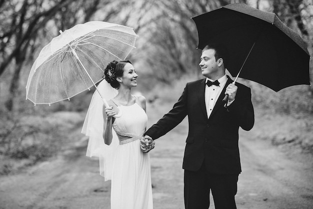 Noiva e noivo em um dia chuvoso de casamento andando sob um guarda-chuva