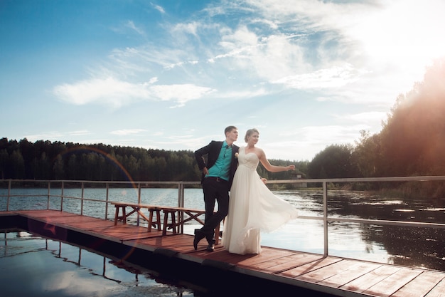 Noiva e noivo estão de pé na ponte no lago. O casal de noivos