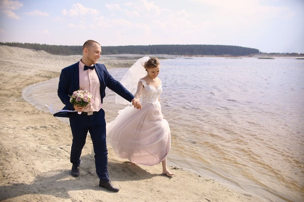Noiva e noivo felizes correndo ao longo do lago da costa
