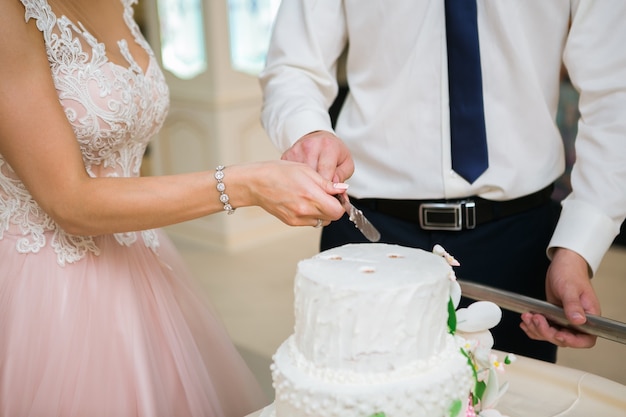 Noiva e noivo na recepção de casamento cortando o bolo de casamento branco