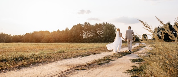 Noiva e noivo no dia do casamento se abraçando e caminhando pela estrada para a floresta ao pôr do sol