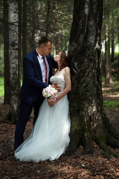 Noiva e noivo se abraçam e se beijam na floresta escura ao sol. casamento na natureza, retrato de um casal apaixonado no parque