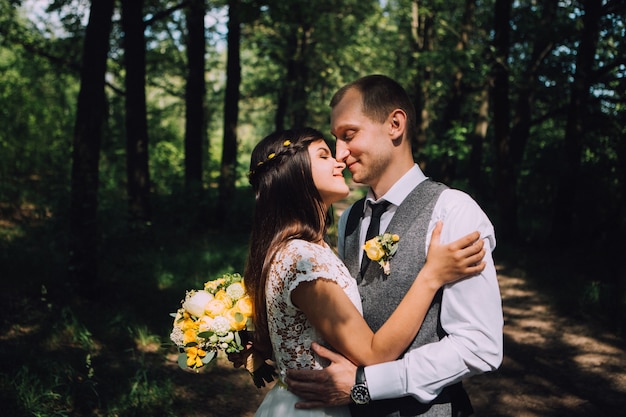 Noiva e noivo se abraçando no dia do casamento, jovem casal feliz se beijando no parque na natureza, dia dos namorados