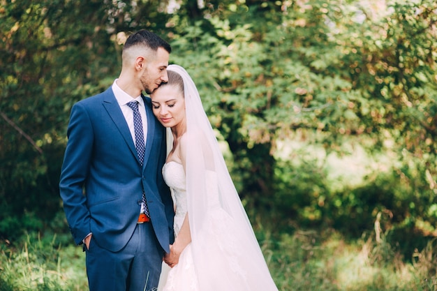 Noiva e noivo se abraçando no dia do casamento, jovem casal feliz se beijando no parque na natureza, dia dos namorados