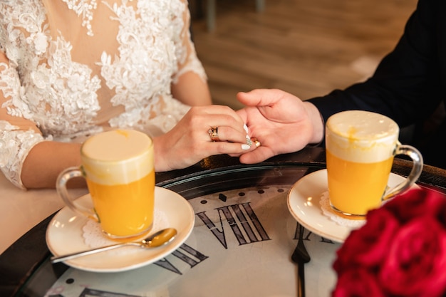 Noiva e noivo segurando as mãos na mesa com relógio perto de cocktails amarelos