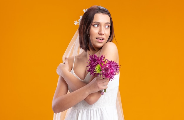 Noiva em um lindo vestido de noiva com buquê de flores olhando para o lado sorrindo alegremente