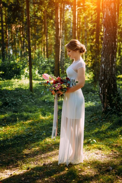 Noiva em um longo vestido branco no parque entre as árvores