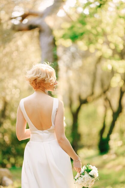 Noiva em um vestido branco com um buquê de flores nas mãos e parada no parque com a cabeça