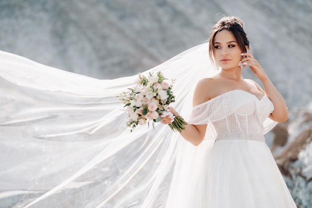 Noiva em um vestido branco com um buquê nas mãos em uma montanha