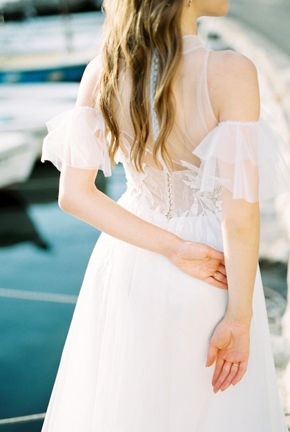 Noiva em um vestido branco fica com as mãos atrás das costas