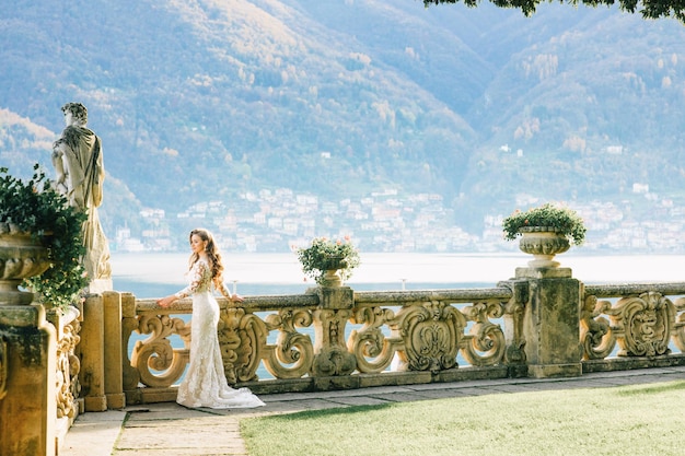 Noiva em um vestido de noiva fica em uma bela varanda com vista para montanhas e lago