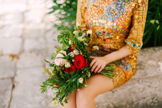 Noiva em um vestido dourado incomum com ícone sentada segurando um buquê de noiva