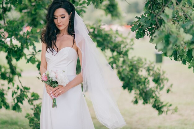 Noiva feliz no lindo vestido branco posando debaixo da árvore.