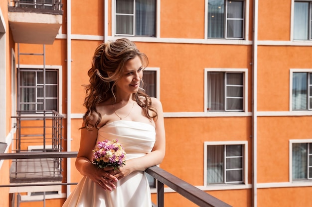 Noiva francesa olhando para longe na varanda com buquê de vestido branco no fundo da casa laranja Retrato nupcial de noiva bonita ao ar livre