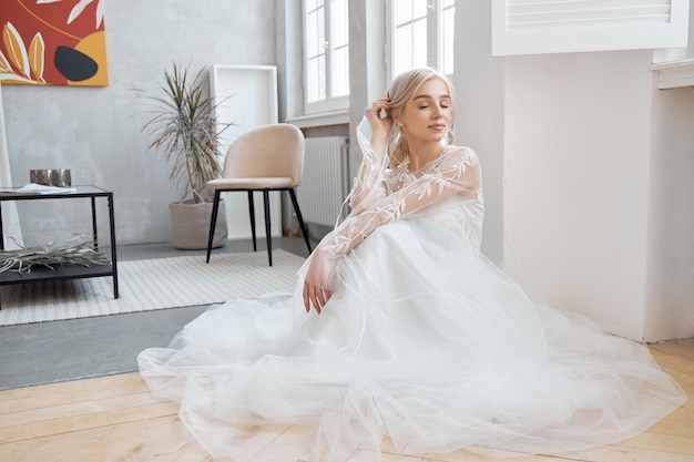 Noiva ideal sentada no chão, retrato de uma menina em um vestido longo branco. Cabelo bonito e pele limpa e macia. Loira penteado de casamento