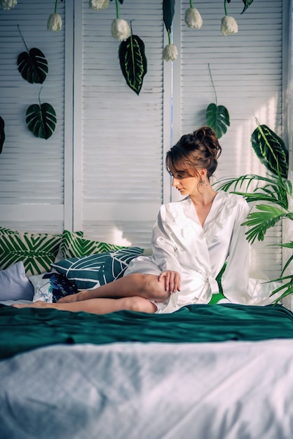 Noiva jovem bonita sentada em uma cama coberta com um cobertor verde em um quarto com flores
