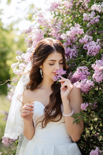 Noiva jovem em um vestido branco em uma floresta de primavera em arbustos lilás