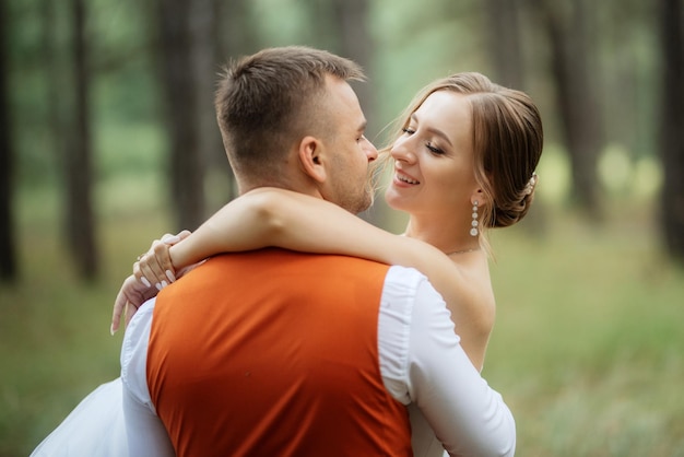 Noiva jovem em um vestido curto branco e noivo em um terno cinza em uma floresta de pinheiros