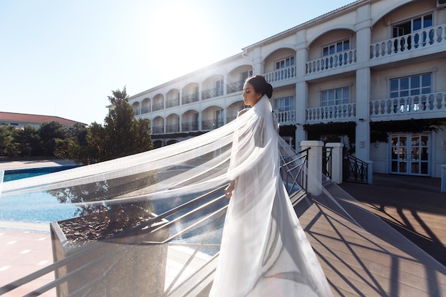 Noiva linda com cabelo escuro em vestido de casamento luxuoso posando na varanda com vista para o mar