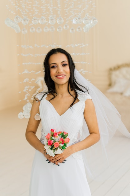 Noiva linda e feliz com seu véu sorrindo e animada em um interior, manhã de casamento