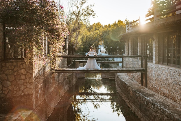 Noiva linda em pé na ponte rústica de madeira na hora do pôr do sol