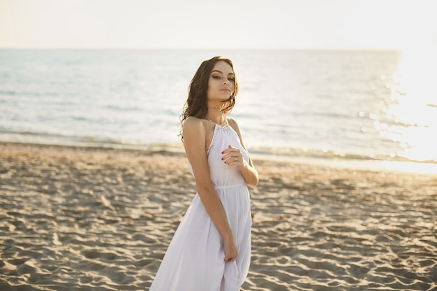 Noiva linda em um vestido branco e tênis, ao pôr do sol caminha ao longo da praia.