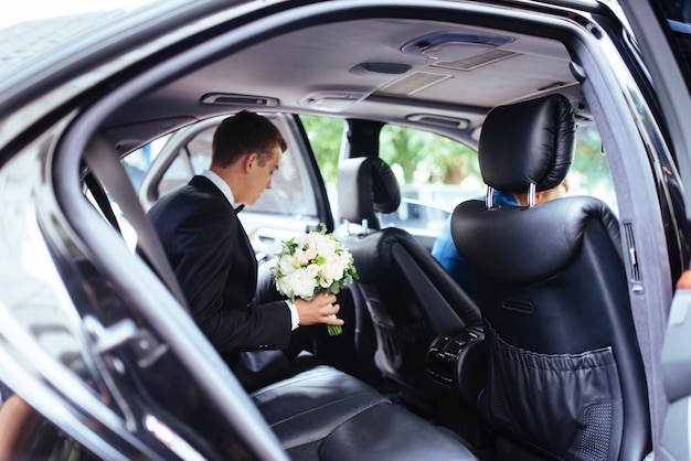 Noiva linda feliz, sentado no carro de casamento com um buquê