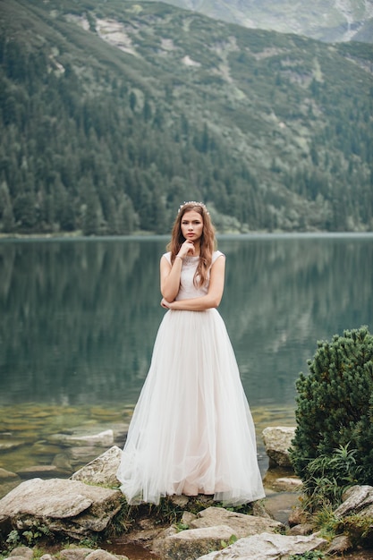 Noiva morena atraente em lindo vestido de noiva branco em pé perto do lago Morskie Oko